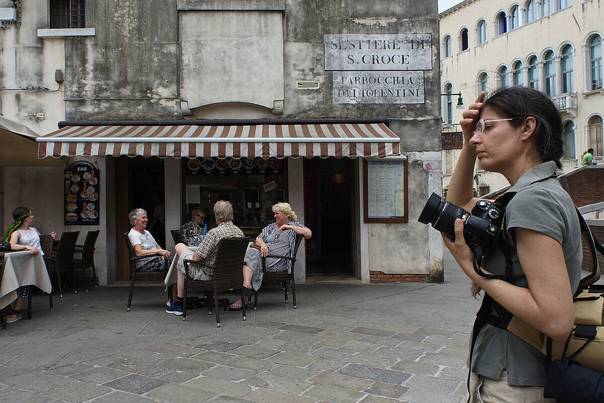 Tired female photographer in front of a bar full of tourists in Venice.