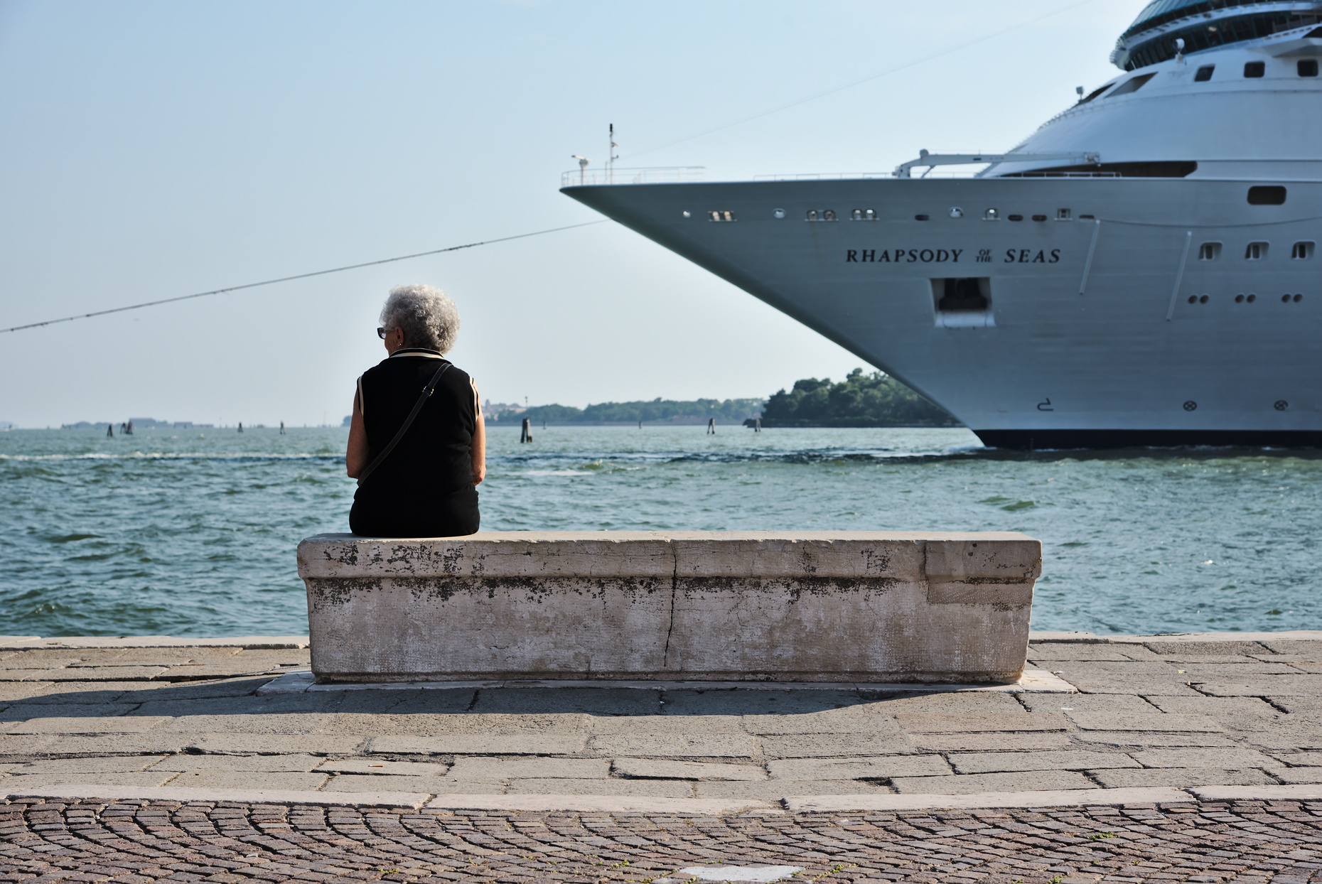 Woman sitting on bench in Venice, with a criuse ship approacing