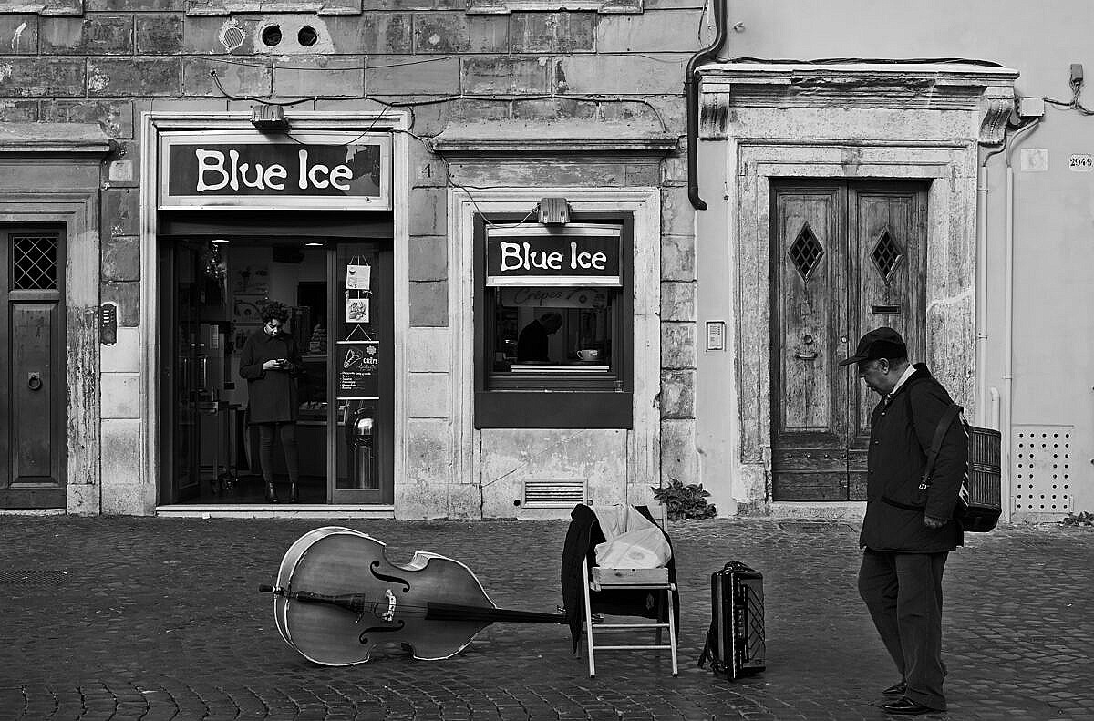 An ice cream parlour in Trastevere in Rome, with musical instruments abandoned one the road and another street musician walking past.