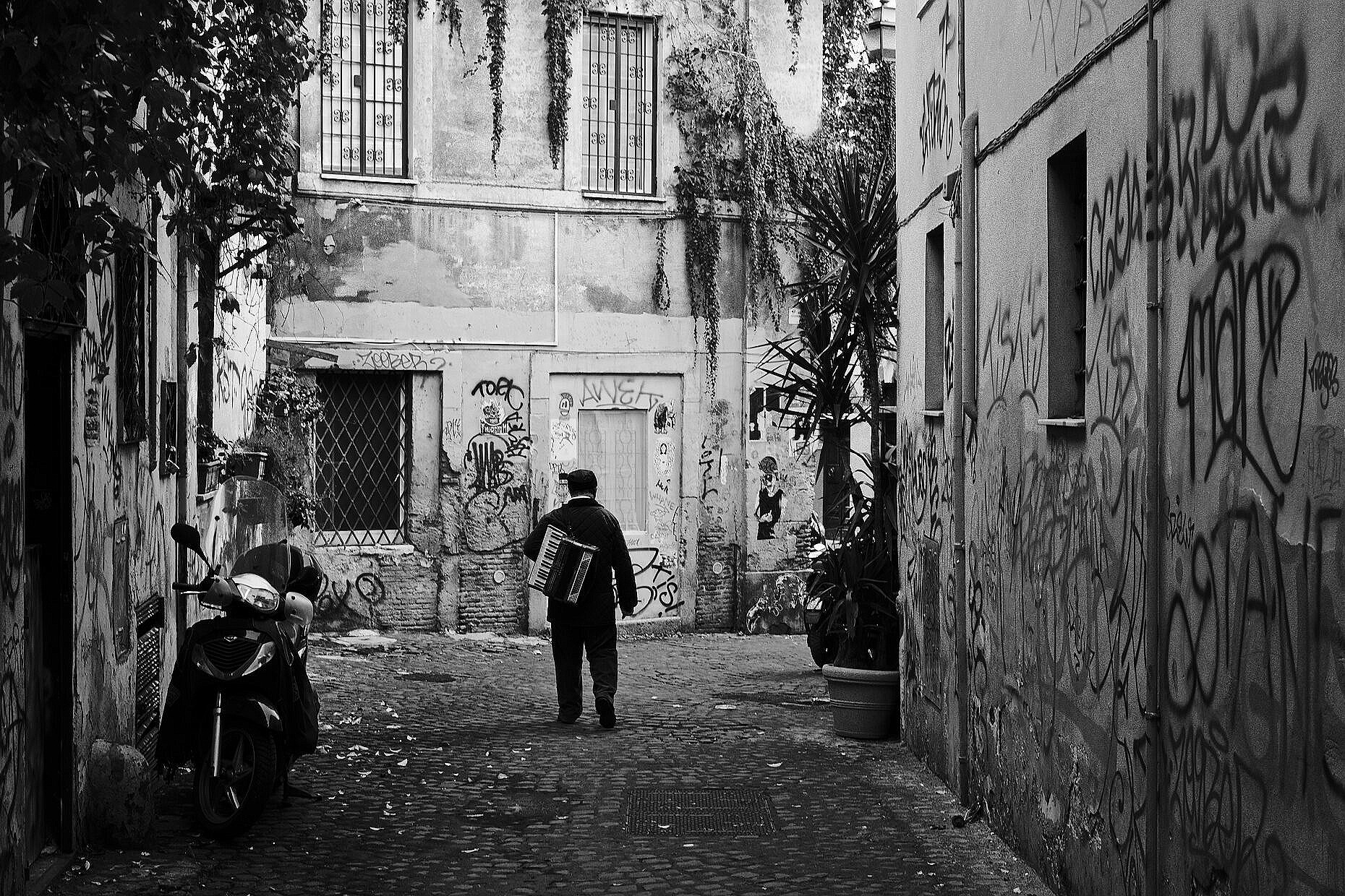 Street musician walking home alone through a picturesque alleyway in Trastevere in Rome.