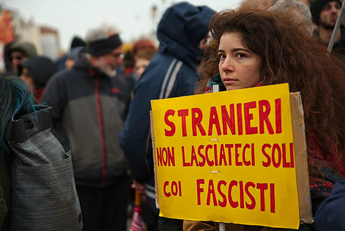 Woman at an anti-fascist demonstration in Venice, with a sign saying "Foreigners. Don't leave us alone with the fascists"