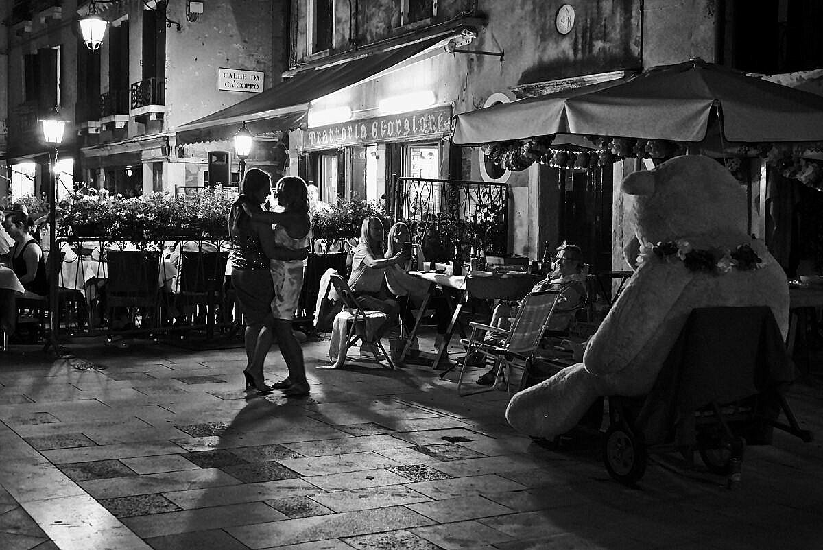 Two women dancing in the Via Garibaldi for the 2017 Redentore feast - with a giant teddy bear watching